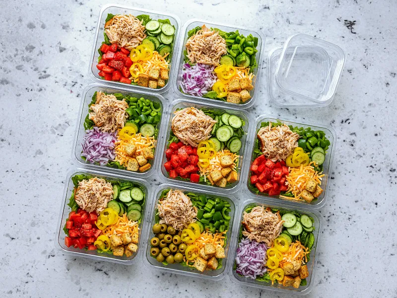 Nine meal-prep salad bowls with shredded chicken and toppings